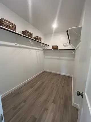 A spacious walk-in closet with wooden flooring, metal hanging rods, and wicker storage baskets.