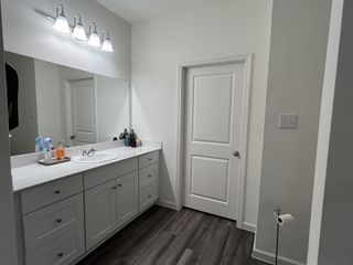 A modern bathroom with a sleek white vanity, spacious mirror, and warm wood floors. Bright lighting enhances its elegance.