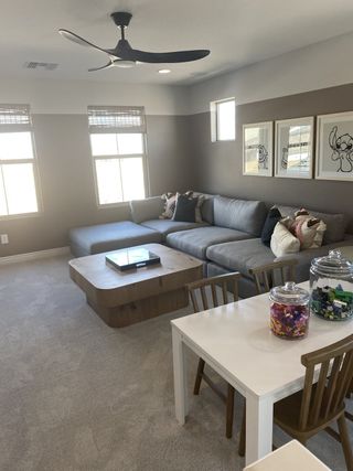 A spacious loft with plush carpet features a gray sectional, modern coffee table, and kids' play area, creating a versatile and comfortable living space.