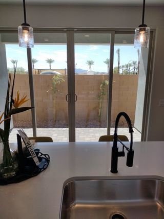 A modern kitchen with a sleek faucet, pendant lighting, and sliding glass doors opening to a patio with palm tree views.