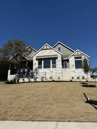 Street view A breathtaking hilltop home with a blend of stone and stucco, framed by mature trees in Lakeside at Tessera by Coventry Homes (Lago Vista, TX).