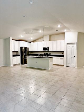 A spacious kitchen with sleek appliances, white cabinetry, and a central island under modern pendant lighting.