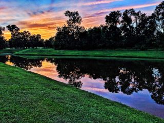 Community Amenities A serene lake reflecting a vibrant sunset with lush greenery in Sienna 80′ by Tri Pointe Homes, Missouri City, TX.