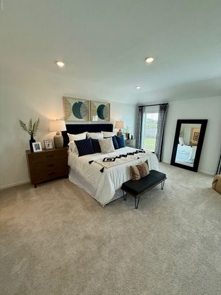 A spacious bedroom with cozy carpeting, modern decor, a stylish bed, and ambient lighting.
