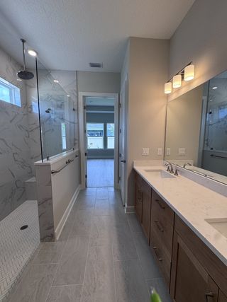 Model Home A modern bathroom featuring a sleek double vanity, glass shower, and elegant tile flooring.