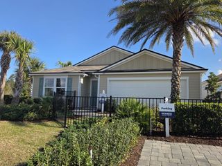 Street view A charming single-story home with siding and a garage in Cross Creek by D.R. Horton (Green Cove Springs, FL) features palm trees and a fenced yard.
