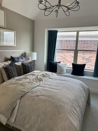 A cozy bedroom with a stylish chandelier, soft bedding, and a charming window seat with accent pillows.