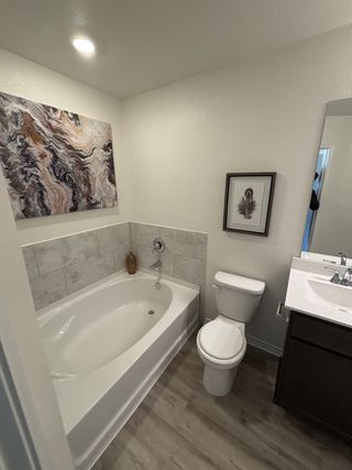 A modern bathroom featuring a sleek tub, elegant artwork, wooden floors, and tasteful lighting.