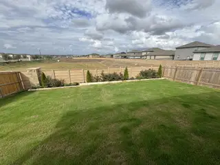 Street view A green backyard with a wooden fence and open views in Cool Water by CastleRock Communities (Jarrell, TX).