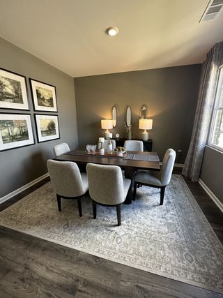 Model Home A cozy dining area with a dark wood table, upholstered chairs, elegant lighting, and framed art.