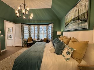 Luxurious bedroom with green walls, plush bedding, large windows, and a chandelier.