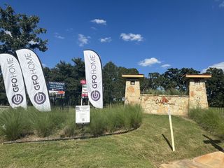 Street view Charming entry to The Oaks Preserve by GFO Home in Eagle Estates, Mansfield, TX, with rustic stone accents and lush landscaping.
