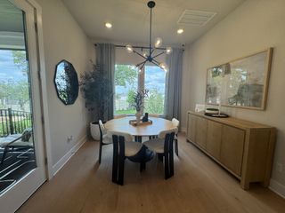 A modern dining room with a round table, chic chandelier, large window, and natural wood sideboard, offering abundant light.
