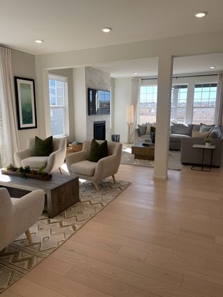 A modern living area with light wood flooring, cozy seating, a stylish fireplace, and large windows.