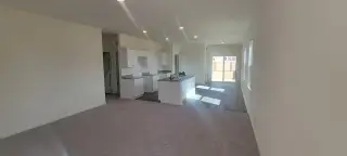 Model Home An open-concept living area with plush carpet, a modern kitchen with white cabinets, and plenty of natural light.