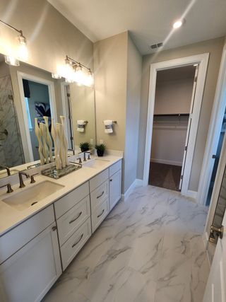 Model Home Modern bathroom with dual sinks, marble-look tiles, elegant lighting, and a spacious walk-in closet.