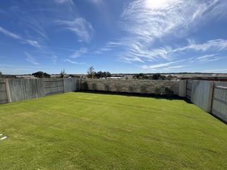Street view A lush green backyard with wooden fencing and open skies in The Cottages at Lariat by Ashton Woods (Liberty Hill, TX).