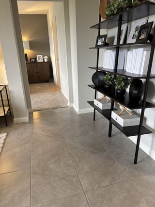 A modern foyer with sleek, tiled floors, decorative shelving, and a view into a cozy carpeted living space.