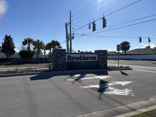 Entrance of Brookhaven by Adams Homes, featuring a stone sign and palm trees under a clear blue sky in Ocala, FL.