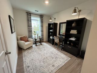 Model Home A cozy home office with a plush armchair, decorative shelving, and a large window filtering natural light.