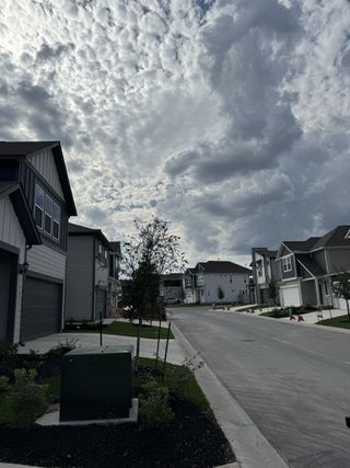Modern homes line a peaceful street under dramatic skies in Sarah's Creek by Taylor Morrison (Pflugerville, TX).