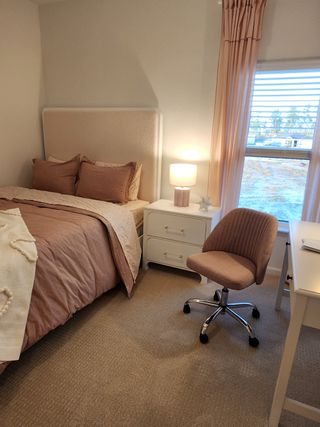 Model Home A cozy bedroom featuring an upholstered bed, soft pink accents, a sleek white desk, and natural light filtering through large windows.