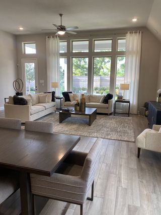 A spacious living area with large windows, light-colored furniture, and hardwood floors, creating an inviting and bright atmosphere.