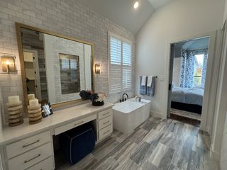 A chic bathroom with a large vanity, gold accents, and a freestanding tub, leading to a bright bedroom.
