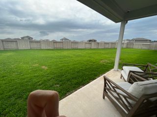 A spacious backyard with a covered patio, ideal for outdoor relaxation, surrounded by lush green grass and a privacy fence.