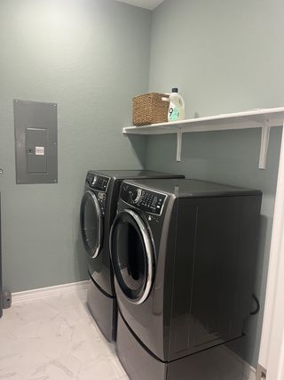 Model Home A modern laundry room with stacked gray Electrolux washer and dryer, a white shelf, and light gray walls offers practical convenience.