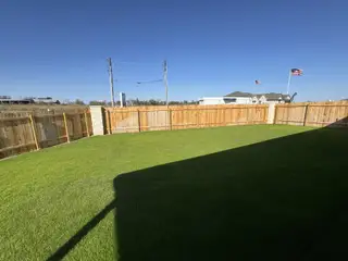 Model Home A spacious fenced backyard with lush grass under a clear sky, perfect for outdoor activities.