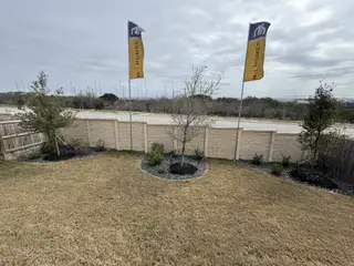 A spacious backyard with flag poles in Hunters Ranch by M/I Homes, featuring neat landscaping in San Antonio, TX.
