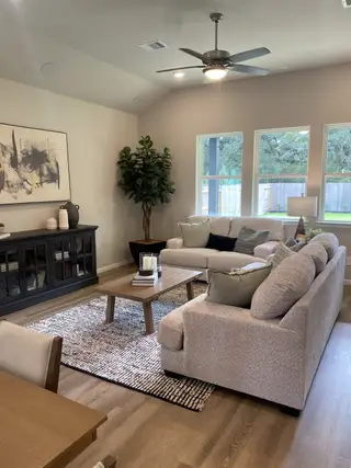 Model Home A cozy living room with plush sofas, hardwood floors, and modern decor, featuring a stylish ceiling fan and large windows.