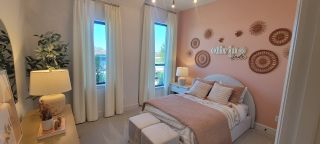 Model Home A cozy bedroom features a blush accent wall, elegant decor, and large windows with white curtains.