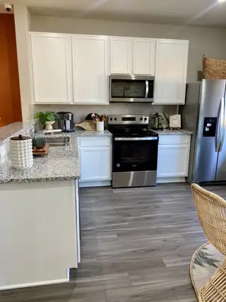 A modern kitchen featuring white cabinets, granite countertops, stainless steel appliances, and wood flooring.