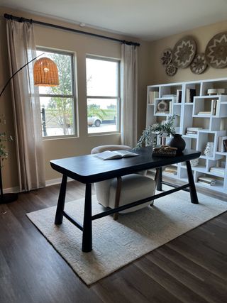 Model Home A cozy home office with a sleek black desk, woven decor, and ample natural light, complemented by a stylish bookshelf.