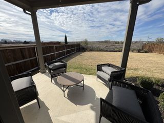 A cozy patio with four gray woven chairs, a round wicker table, a ceiling fan, and a view of a fenced backyard with dry grass and a clear blue sky.