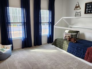 Model Home A cozy children's room features a house-shaped bedframe, plush toys, and navy curtains complementing the bright, airy space.