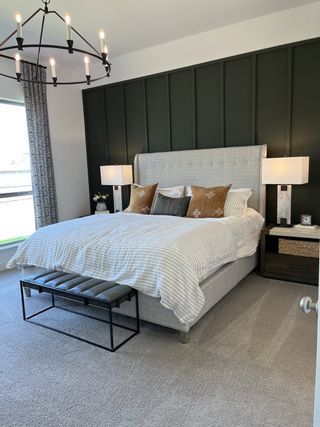 A modern bedroom featuring a tufted headboard, dark accent wall, elegant chandelier, and cozy decor.