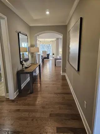 A welcoming hallway featuring wooden floors, a sleek console table, modern art, and a bright view into the living area.