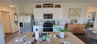 A bright kitchen with white cabinets, stainless steel appliances, and a granite island flows into an open living space with rustic decor.