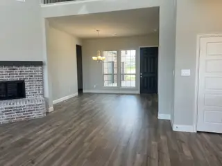An elegant open living area with wood flooring, a brick fireplace, and ample natural light and overhead lighting.