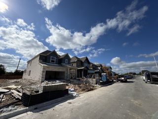 Street view New construction homes in South Brook by David Weekley Homes, Leander, TX, under a vibrant, cloud-dotted sky.