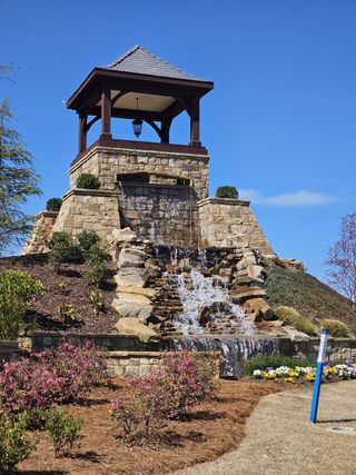 A charming stone structure with a cascading waterfall and lush landscaping in Braselton Village by D.R. Horton (Braselton, GA).
