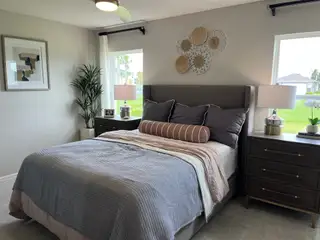 Model Home A cozy bedroom featuring a plush bed, elegant decor, and natural light from large windows for a serene vibe.