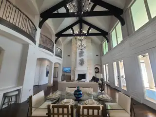 An elegant living room with vaulted ceilings, exposed beams, and a grand fireplace, featuring a stylish dining area.