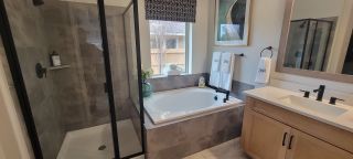 Model Home A luxurious bathroom with a soaking tub, a glass-enclosed shower, and dual sinks with black fixtures for a sleek modern touch.