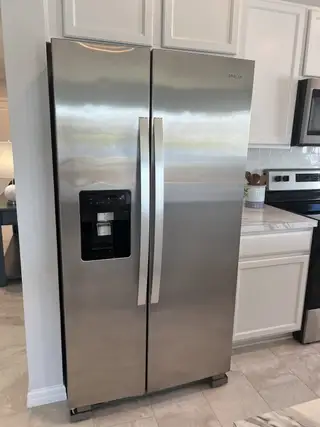 A sleek stainless steel refrigerator with a water dispenser, set against white cabinetry in a modern kitchen.