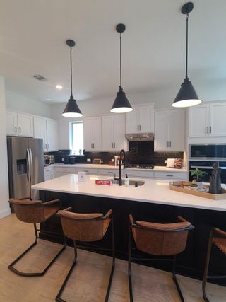 A contemporary kitchen with sleek black pendant lights, white cabinetry, and a spacious island featuring stylish bar stools.
