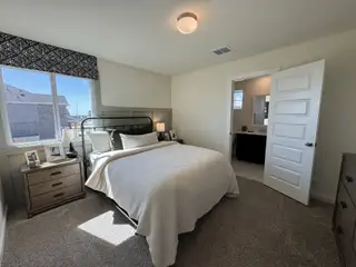 Model Home A cozy bedroom with neutral tones, a metal bed frame, carpeted flooring, and elegant decor.